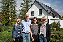 Familie Klau vor ihrem Eigenheim mit Photovoltaik-Anlage auf dem Dach.