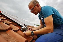 Handwerker schließt einen Kollektor für eine Solarthermieanlage auf dem Dach an.