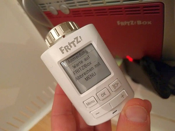 Smartes, weißes Thermostat in der Hand vor rotem Router: AVM Fritz!DECT 301 und AVM FritzBox